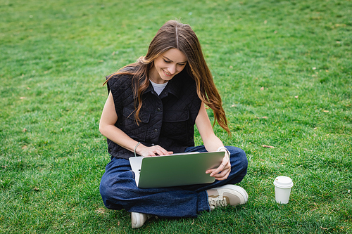 happy young woman using laptop while sitting on lawn