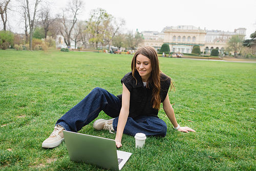 smiling young woman using laptop while sitting on lawn