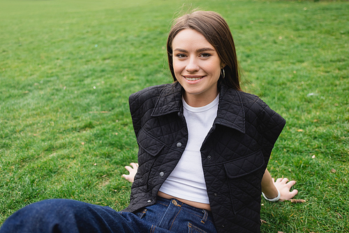 smiling young woman in sleeveless jacket sitting on lawn