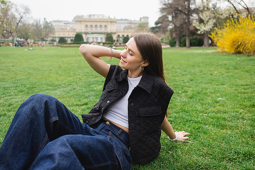 happy young woman in sleeveless jacket sitting on lawn