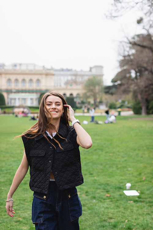 young cheerful woman in sleeveless jacket in green park