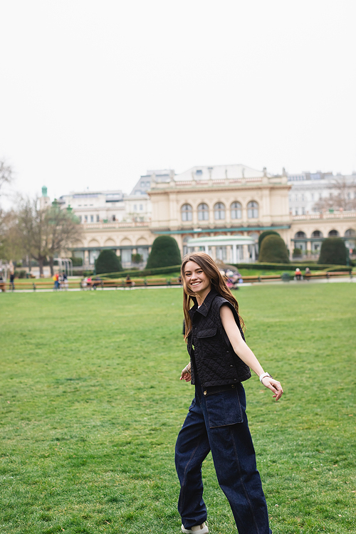 young joyful woman in sleeveless jacket in green park