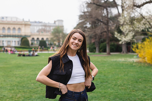 young and smiling woman in sleeveless jacket in green park