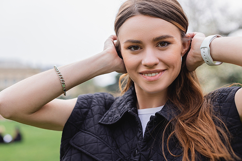 young cheerful woman in sleeveless jacket adjusting hair