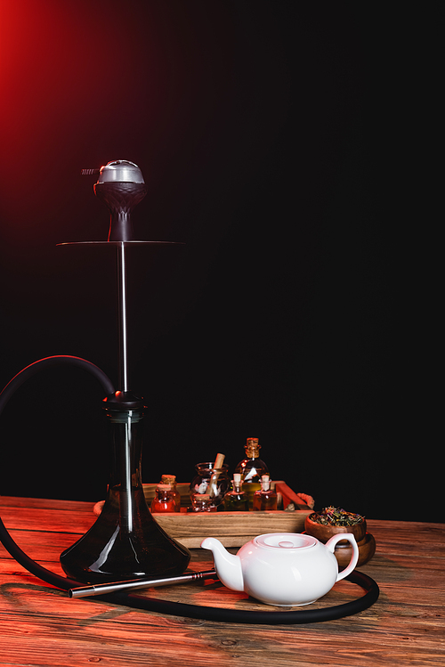 Hookah near teapot and jar on wooden surface on black background