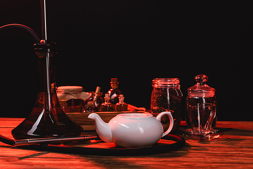 Hookah near teapot and jars on wooden surface isolated on black