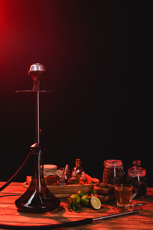 Hookah, tea and limes on wooden surface on black