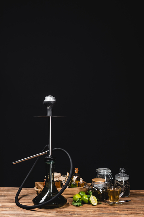 Hookah, limes and tea on wooden surface isolated on black