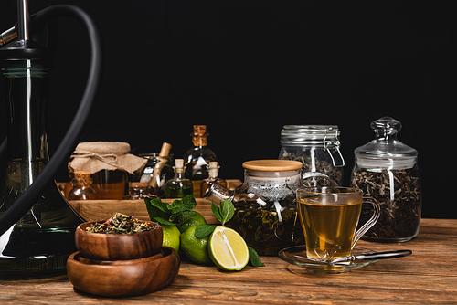 Dry tea, limes near hookah on wooden surface isolated on black