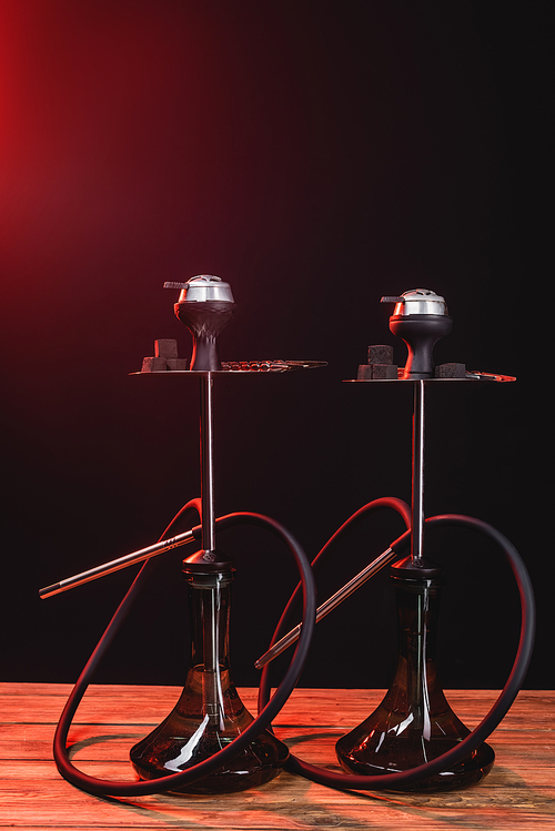 Hookahs on wooden surface on black background with red light