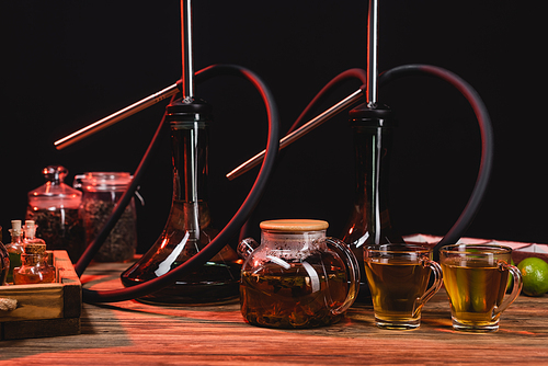 Tea in teapot, lime and hookahs on wooden surface isolated on black