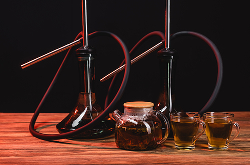 Teapot near hookahs on wooden table isolated on black