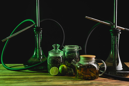 Dry tea, teapot and hookahs on wooden surface isolated on black