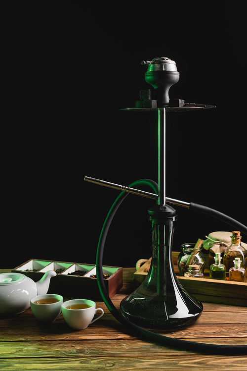 Hookah near tea on wooden table isolated on black