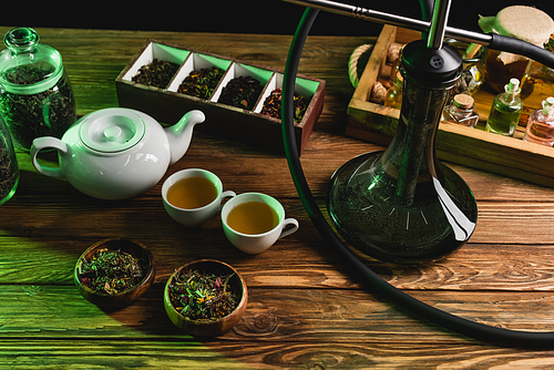 Top view of teapot, dry tea and hookah on wooden surface isolated on black