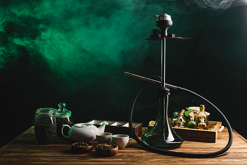 Tea and hookah on wooden table on black background with smoke