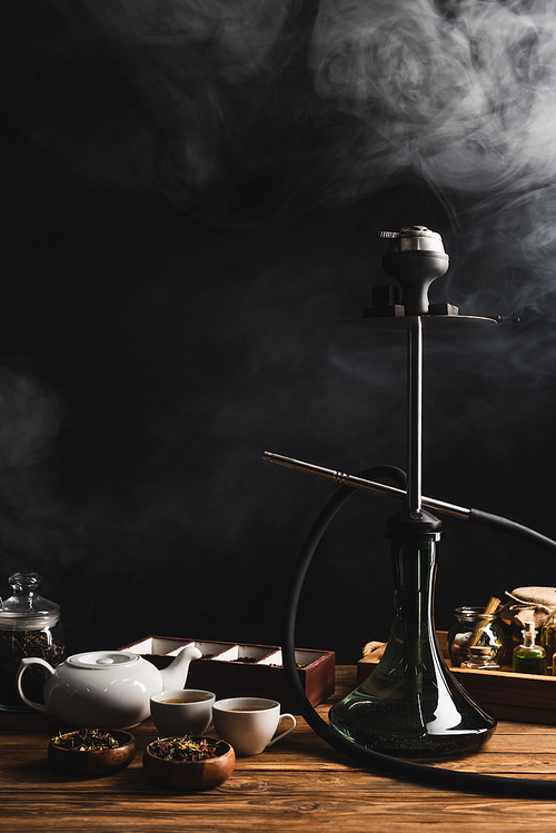 Hookah, tea and teapot on black background with smoke