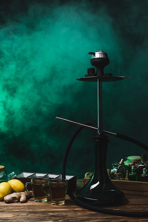 Hookah, lemons and tea on wooden surface on black background with smoke