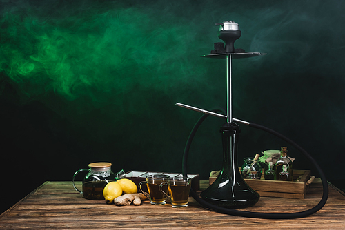 Lemons, tea and hookah on wooden surface on black background with smoke