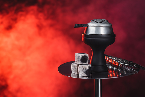 Coals and tweezers on hookah on black background with red smoke