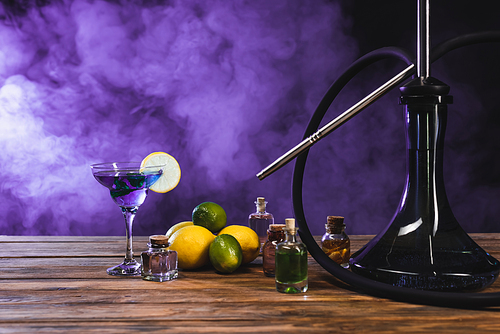 Hookah near fruits and cocktail on black background with purple smoke