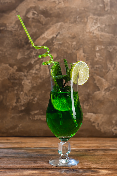 glass of green cocktail with  straw on wooden surface on textured stone background