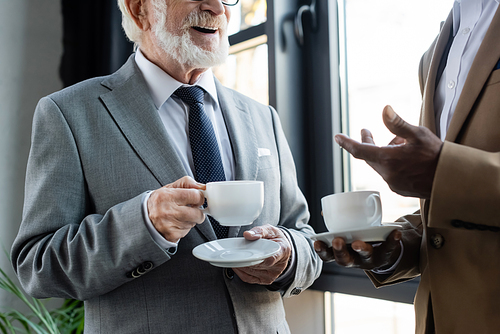 cropped view of senior businessman standing near african american colleague during coffee break