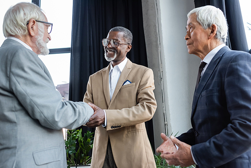 senior asian businessman looking at business partners shaking hands in office
