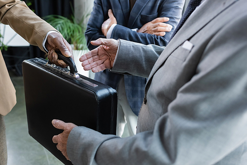 partial view of african american man giving briefcase to business partner in office