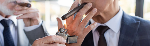 partial view of blurred businessman lighting cigar of senior business partner, banner