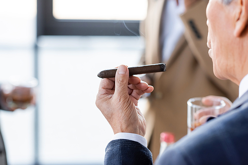cropped view of senior businessman smoking cigar in office