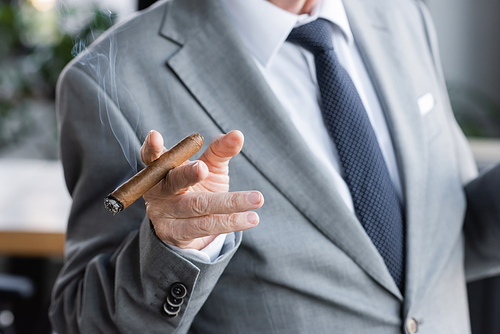partial view of senior businessman in suit holding cigar in office