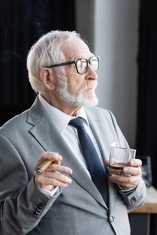 elderly businessman with cigar and glass of whiskey looking away in office