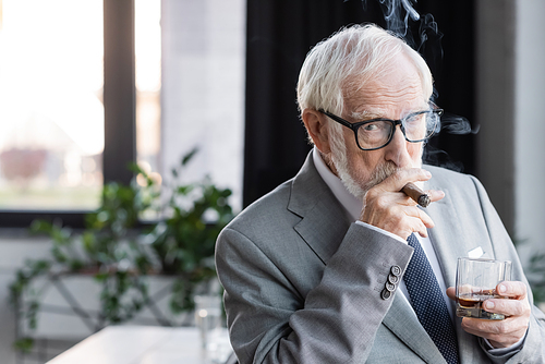 elderly businessman with glass of whiskey  while smoking cigar in office