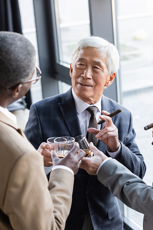 senior asian businessman smiling while clinking glasses of whiskey with business partners