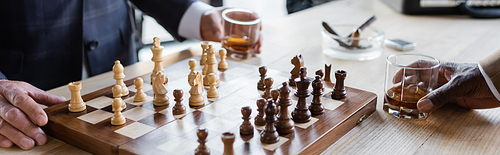 cropped view of business partners with glasses of whiskey playing chess in office, banner
