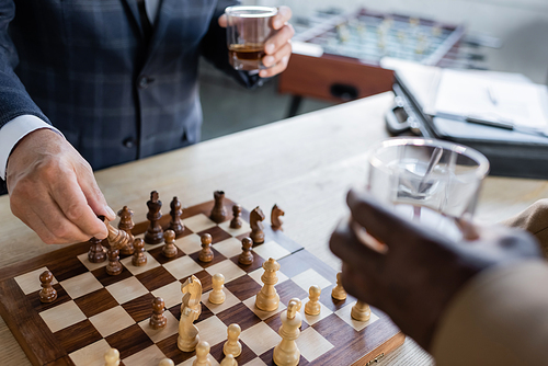 partial view of blurred senior businessmen with glasses of whiskey playing chess in office