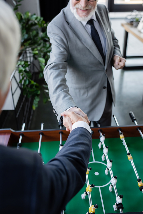 cropped view of senior businessman shaking hands with blurred colleague near table football