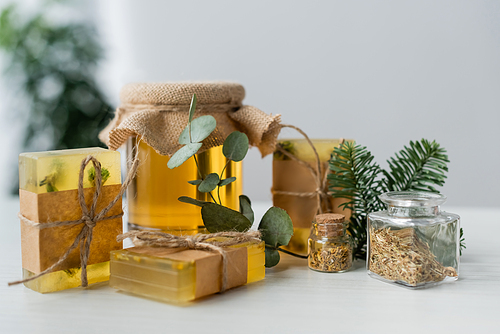 Handmade soap bars near honey, eucalyptus and herbs on table