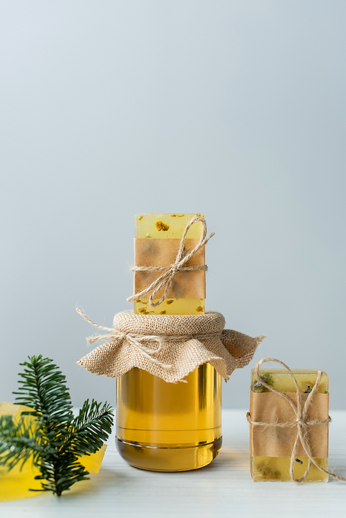 Handmade soap on jar with honey near spruce branch on grey background