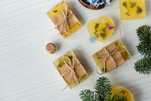 Top view of handmade soap bars near flowers and pine branches on table