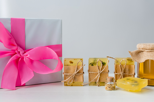 Gift box near handmade soap bars and jar with honey on grey background