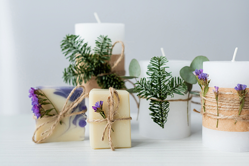 Craft soap bars near candles with spruce branches on grey background