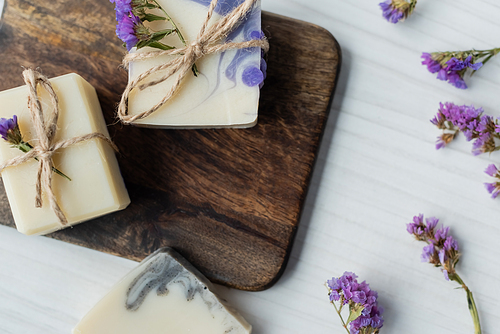 Top view of handmade soap bars on cutting board near dry flowers on table