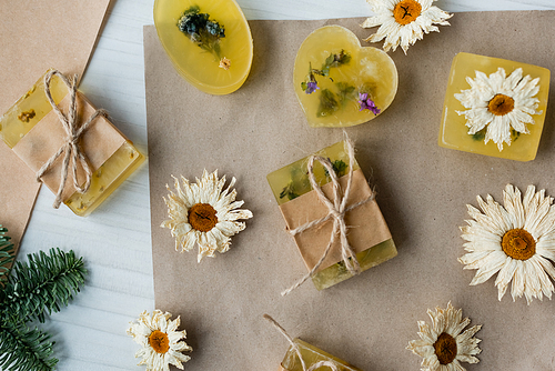 Top view of handmade soap near dry chamomiles on craft paper on table