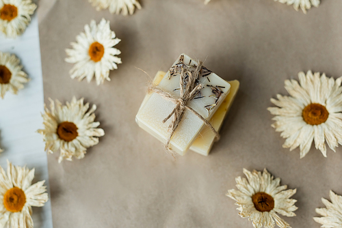 Top view of handmade soap with twine near chamomiles on craft paper