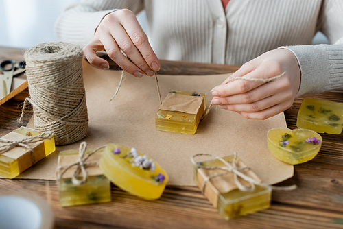 Cropped view of craftswoman holding twine near handmade soap on craft paper