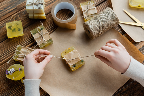 Top view of craftswoman holding twine near craft soap on paper at home