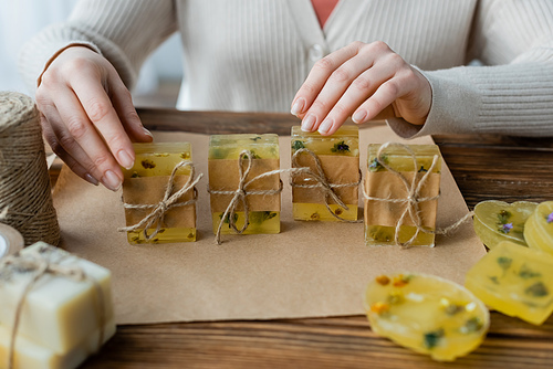 Cropped view of craftswoman touching handmade soap bars near twine and craft paper at home