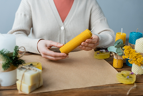 Cropped view of craftswoman holding handmade candle near soap and craft paper on table